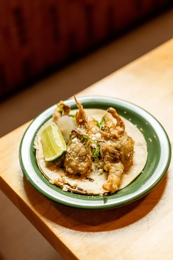 Two soft-shell crab tacos with cheese, herbs, radish, and lime.