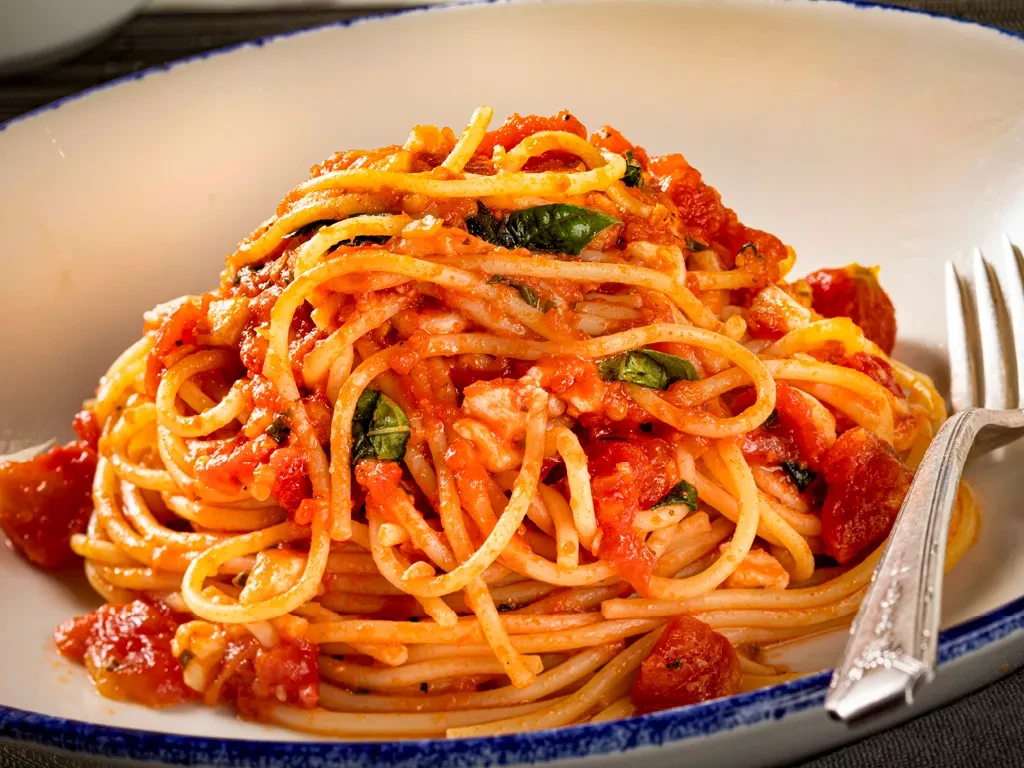 Bowl of spaghetti with tomato sauce, basil, and a silver fork.