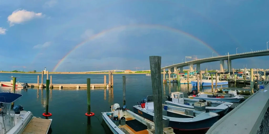 Marina with boats, a multi-span bridge, and a vibrant double rainbow.