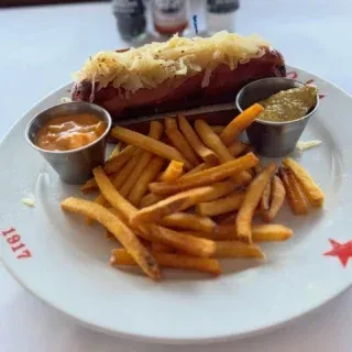 Hot dog with sauerkraut, fries, and two sauces on a white branded plate.