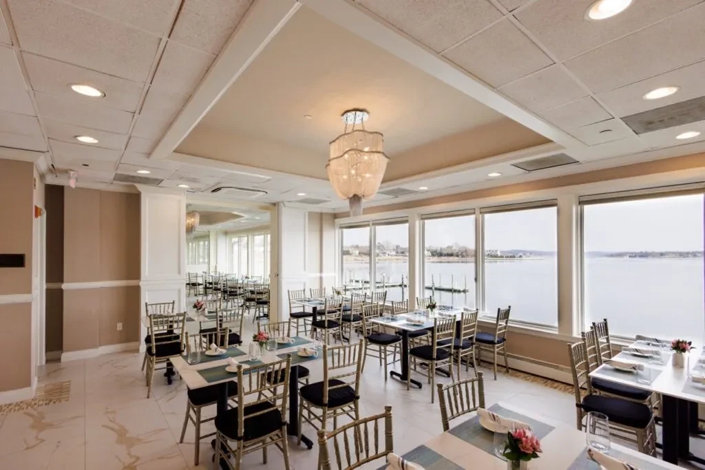 Elegant dining room with set tables, a chandelier, and waterfront view.