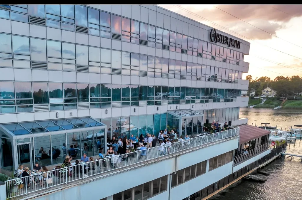 Modern, reflective 'The Oyster Point' building, lively waterfront dining at sunset.
