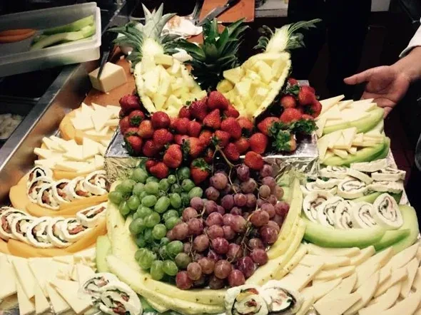 Extensive fruit, cheese, and appetizer buffet with a visible hand.