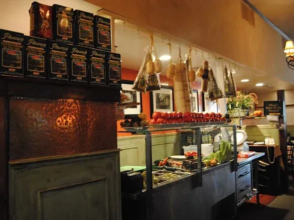 Rustic restaurant deli counter with fresh ingredients, hanging meats, olive oil.