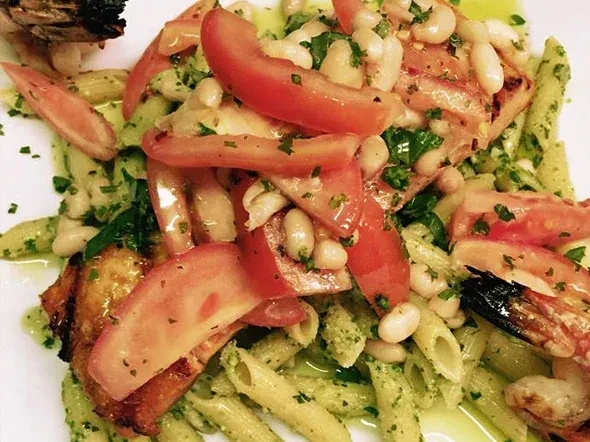 Penne pasta with vibrant green pesto, red tomatoes, white beans, and shrimp.