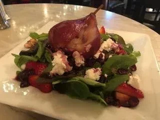 Plated dark red poached pear salad with greens, cheese, and fruit.