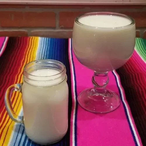 Milky drinks in mason jar and stemmed glass on colorful serape.