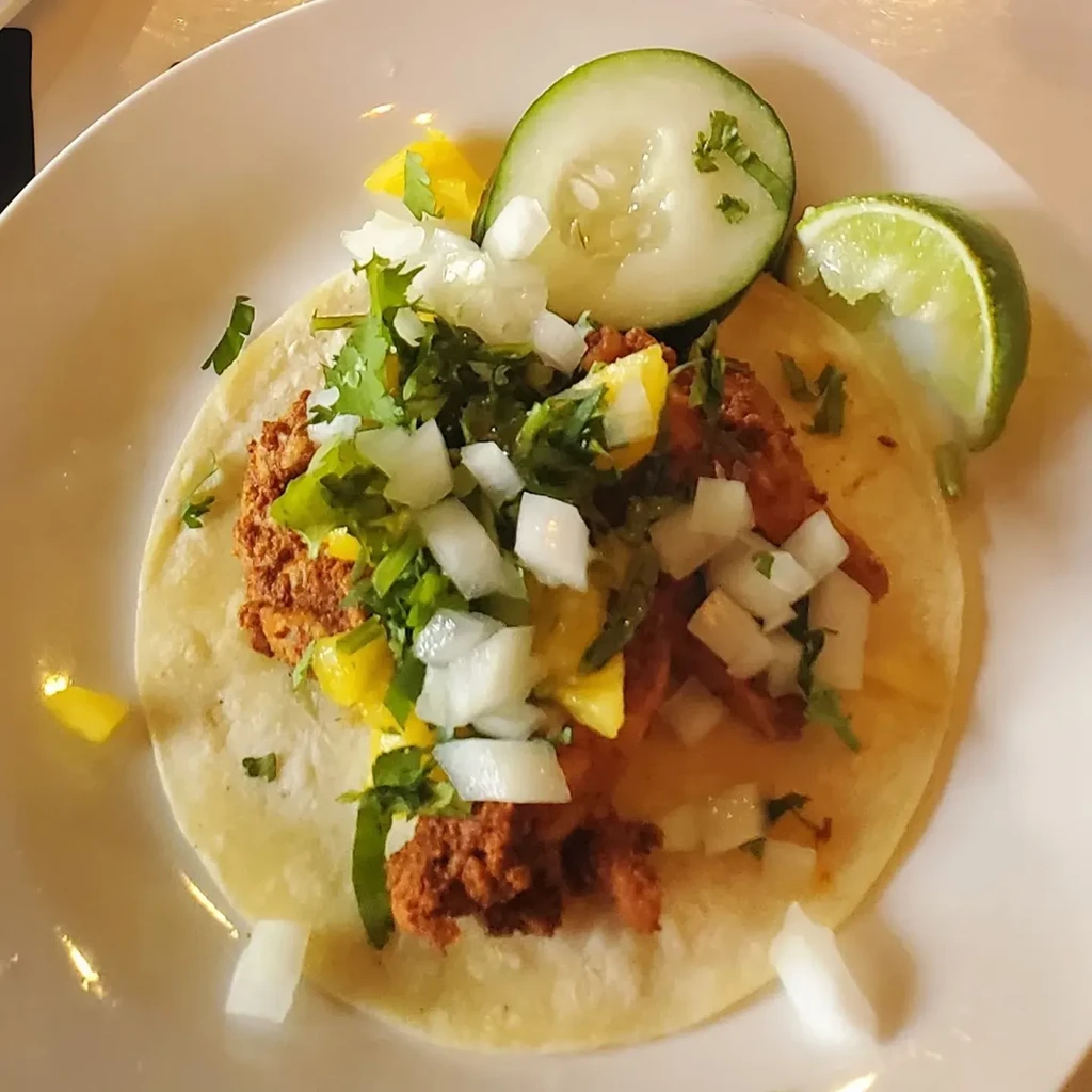 Overhead view: Meat taco with fruit, onion, cilantro, cucumber, lime.
