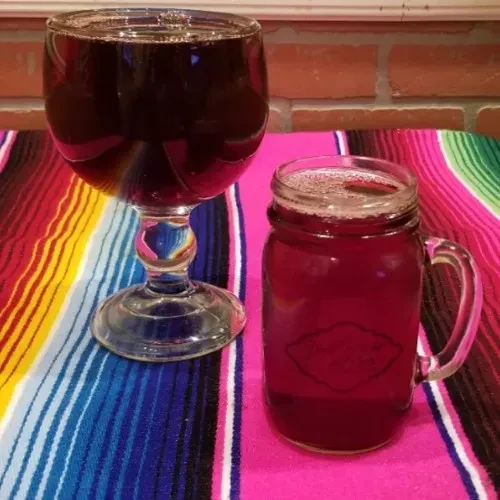 Two reddish beverages in glass on a vibrant striped background.