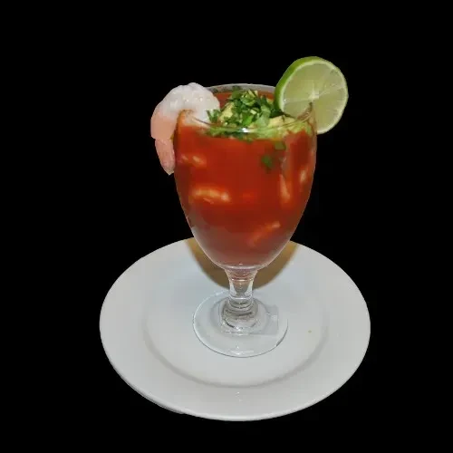 Shrimp cocktail in a stemmed glass, garnished with lime, herbs, and shrimp.