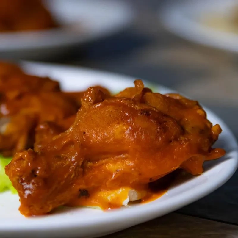 Close-up of fried chicken wing coated in glossy orange-red sauce.