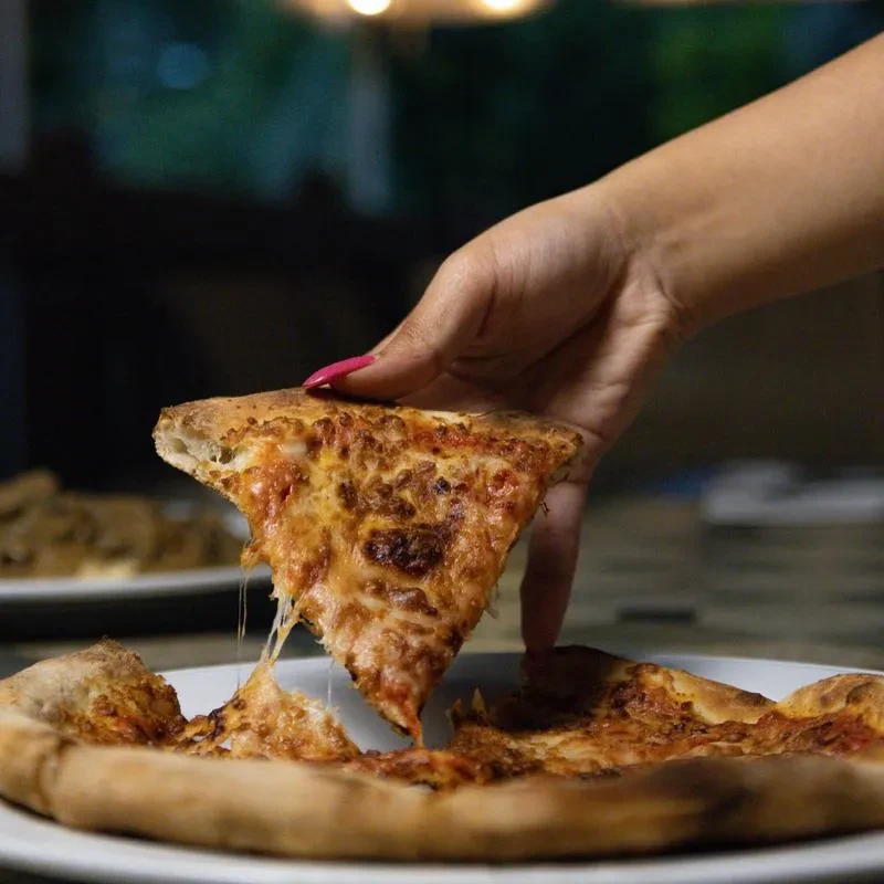 A pink-polished hand lifts a hot, cheesy pizza slice, melting cheese.