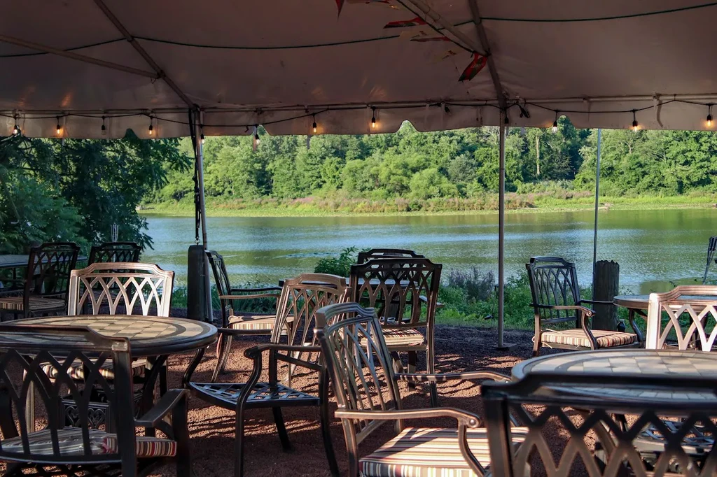 Empty tented outdoor dining area beside a lake and trees.