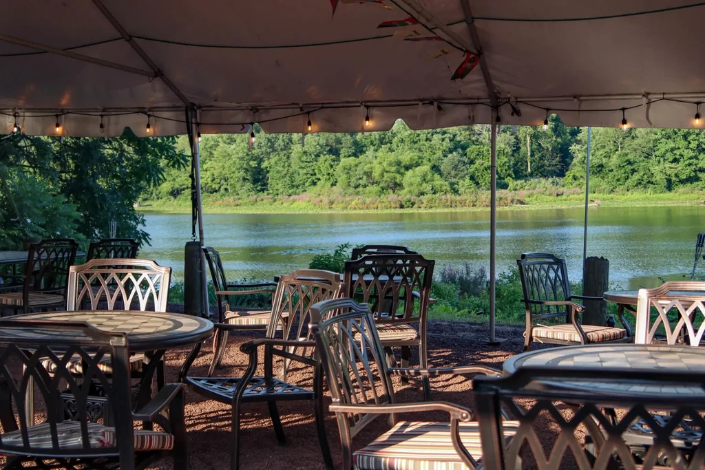 Outdoor dining under white tent with dark furniture and water view.