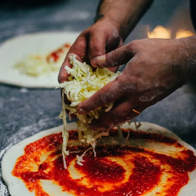 Close-up: Chef's hands sprinkling cheese onto a pizza with tomato sauce.