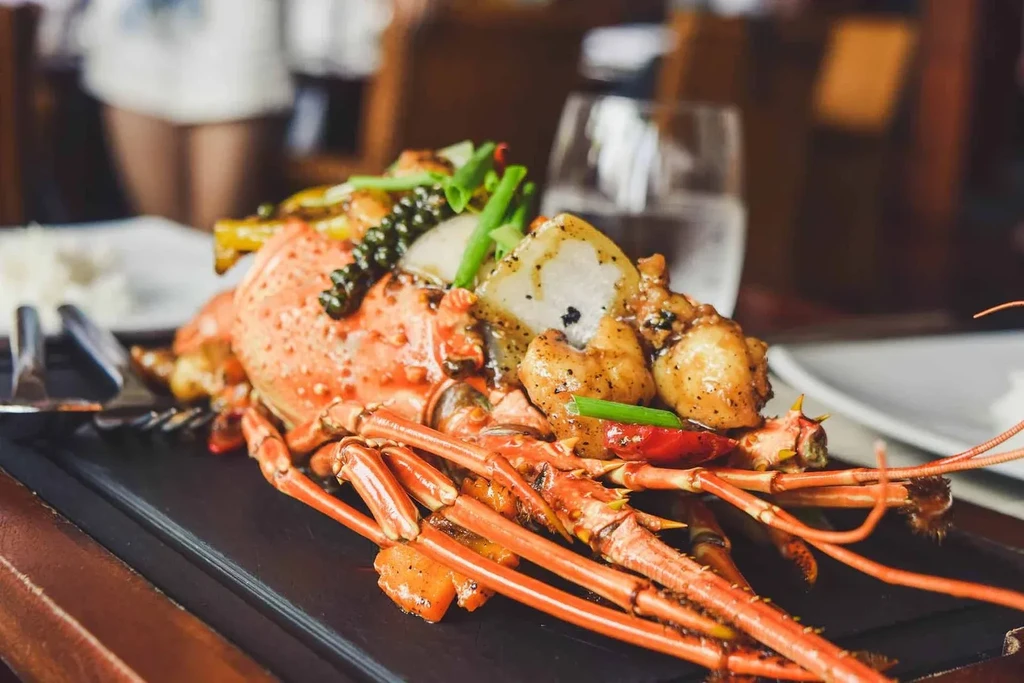 Vibrant sauced lobster garnished with peppercorns, green onions, and chili peppers.
