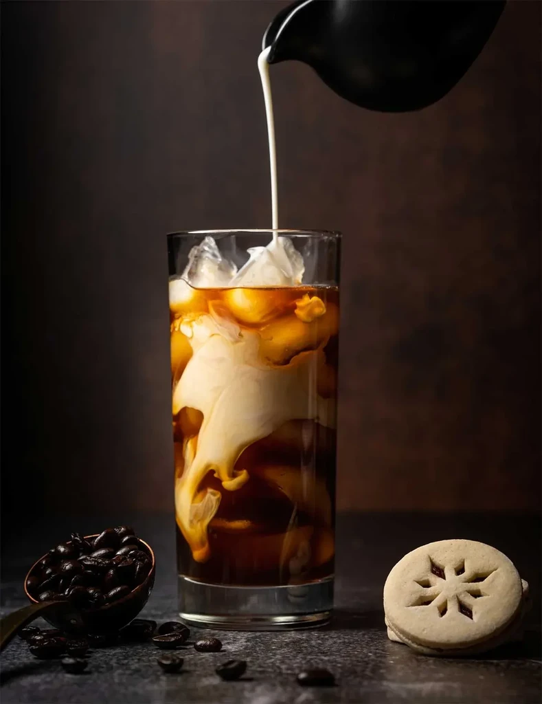 Iced coffee with pouring milk, coffee beans, and a snowflake cookie.