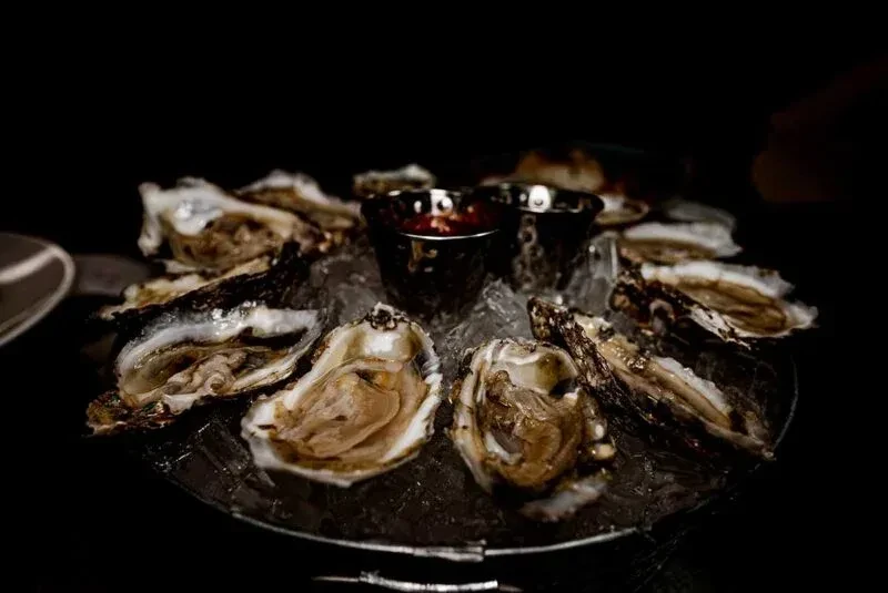 Platter of shucked oysters on ice with a reddish sauce.