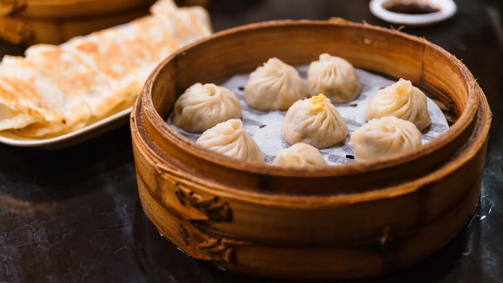 Eight steamed dumplings in a bamboo steamer, with flatbread and sauce.