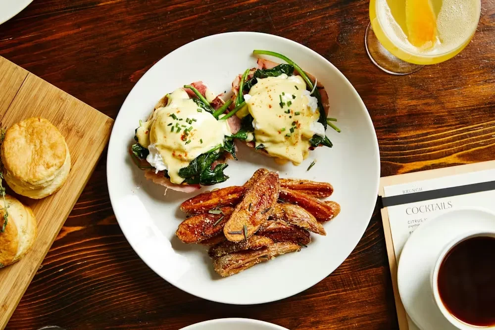 Overhead view: Eggs Benedict, biscuits, cocktail, and coffee on table.