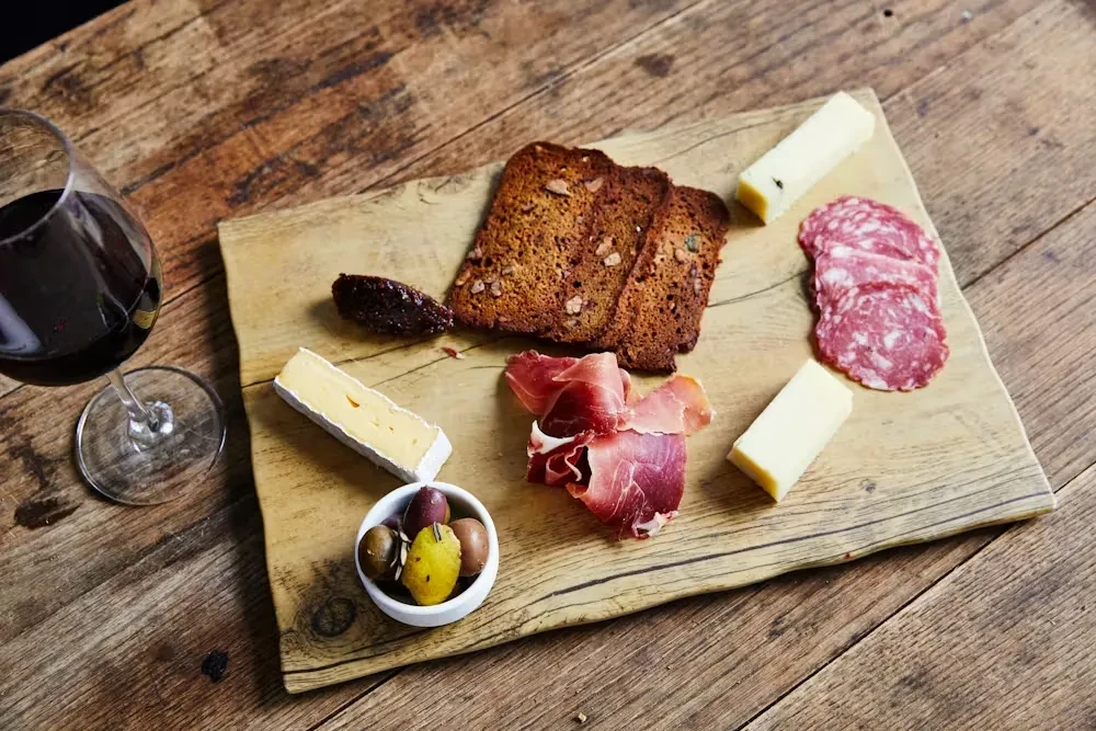 Charcuterie board with cheeses, cured meats, bread, olives, and red wine.