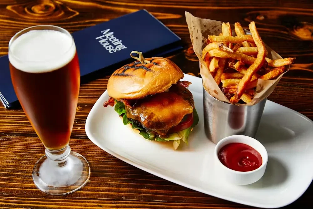 Gourmet burger, fries, and beer on a dark wooden table.