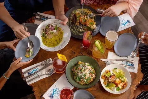 Overhead: many hands reaching for various dishes and drinks.