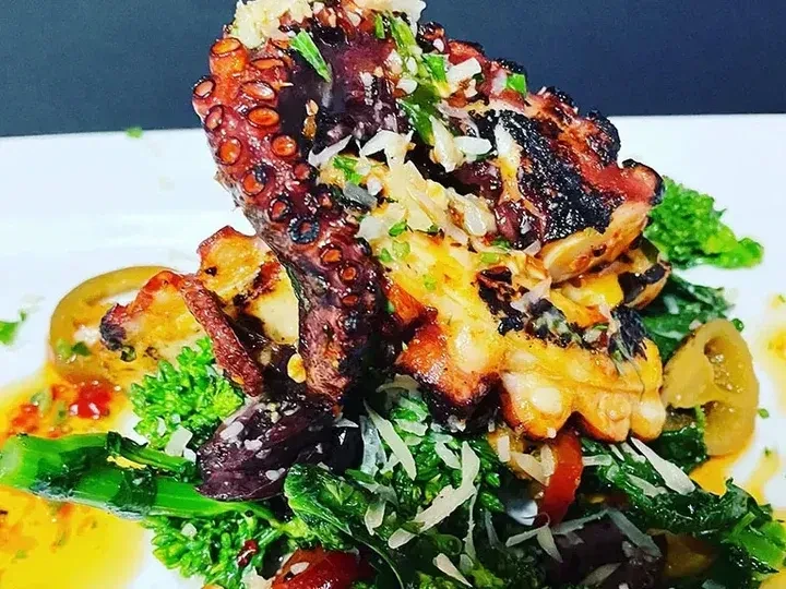 Grilled octopus with herbs, cheese, green vegetables, and a rich sauce.