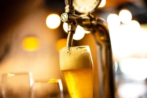 Metallic beer tap actively pouring golden beer into a tall glass.