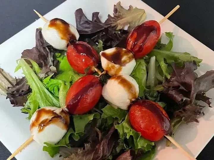 Caprese skewers with mozzarella, tomatoes, balsamic glaze, on mixed greens.