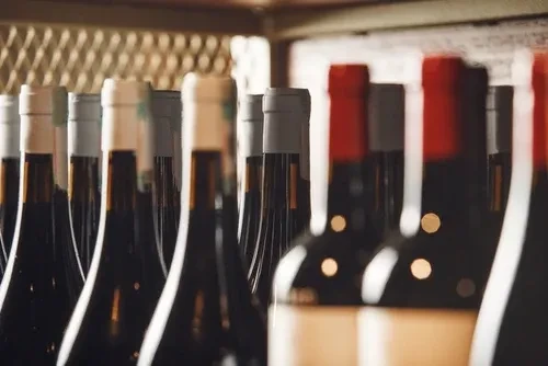 Rows of dark wine bottles with red and light caps, dimly lit.