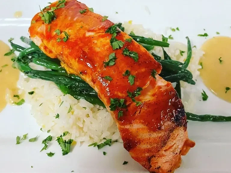 Professionally plated glazed salmon, rice, green beans, and sauce.