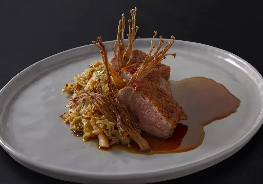 Seared duck breast, roasted cabbage, enoki mushrooms, and sauce on a plate.