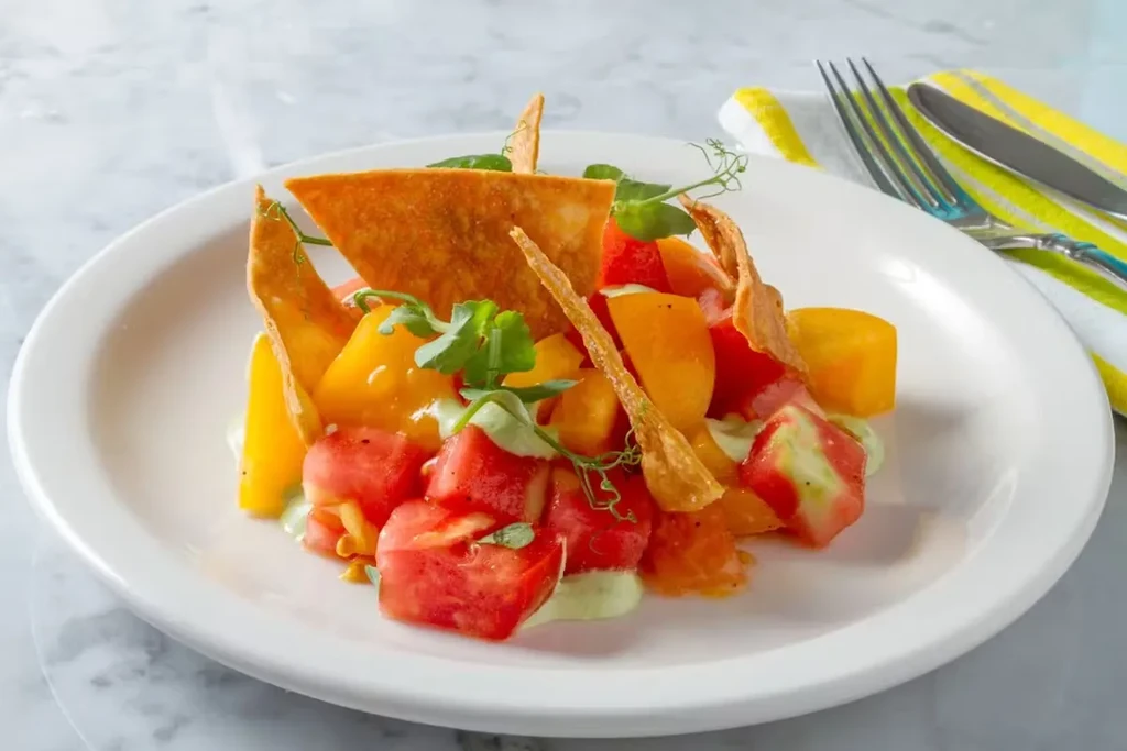 A dish with chopped tomatoes, watermelon, chips, and green sauce.