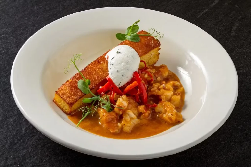 Fried cornbread with stew and toppings on a white plate.