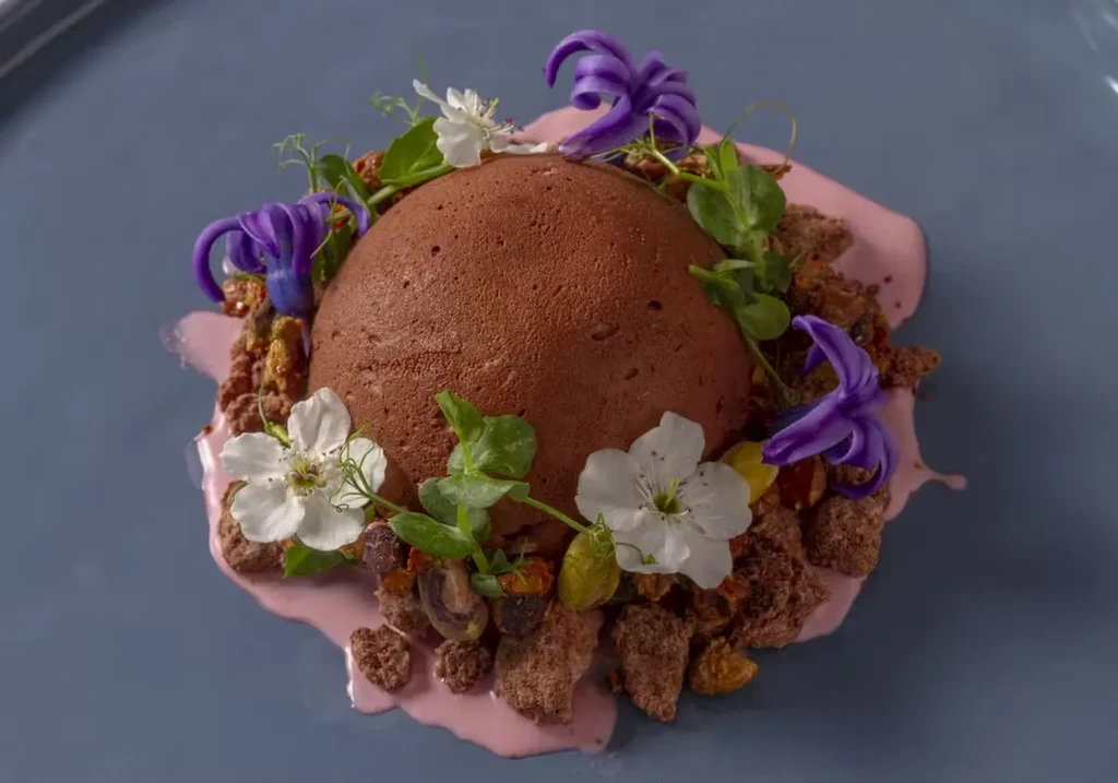 A chocolate dessert, garnished with flowers and pink sauce, on a gray plate.