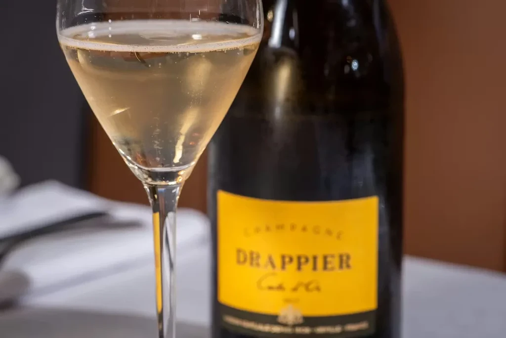 Effervescent champagne in a flute next to a DRAPPIER bottle.