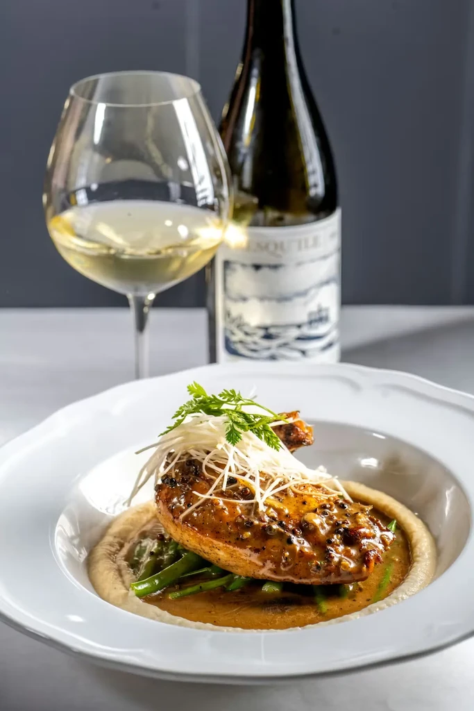 Elegant seared chicken/fish dish with sauce, vegetables, and wine.