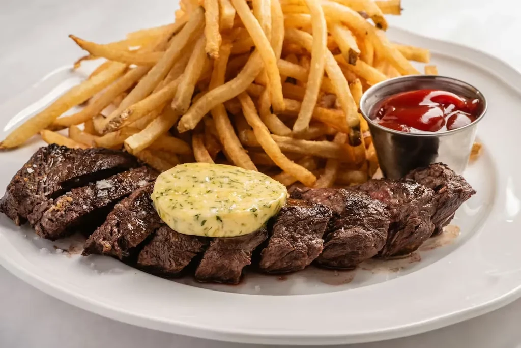 Plate of sliced medium-rare steak frites with herb butter and ketchup.