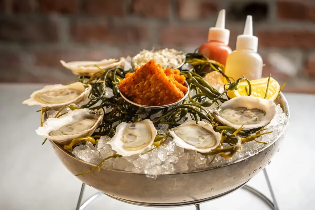 Fresh oysters on ice with seaweed, lemon, sauces, and accompaniments.