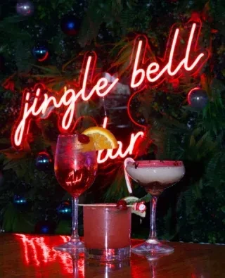 Three festive drinks, "jingle bell bar" neon sign, Christmas tree.