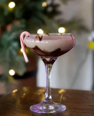 Holiday drink in coupe glass with chocolate drizzle and candy cane.