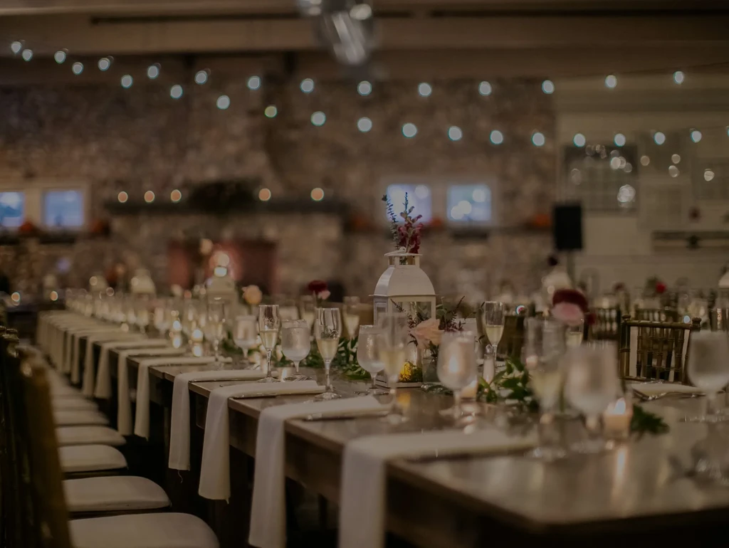 Elegantly set long dining table with candles and flowers; rustic venue.