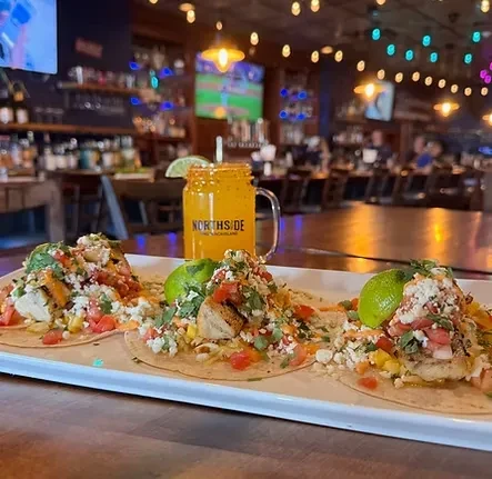 Three generously garnished tacos with a NORTHSIDE orange drink.
