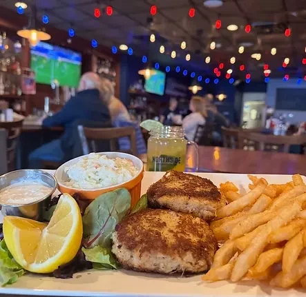 Golden-brown crab cakes and fries with coleslaw served in a lively bar.