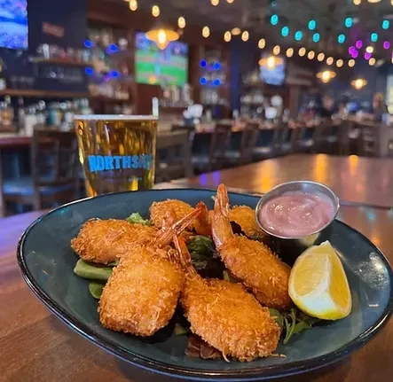 Fried shrimp plate with sauce, lemon, and beer at a bar.