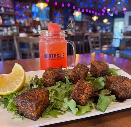 Plate of seasoned protein, greens, lemon, and a Northside Long Beach Island drink.