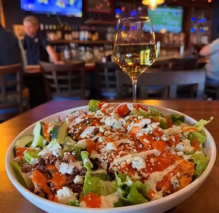 Large buffalo chicken salad, wine glass, restaurant background.