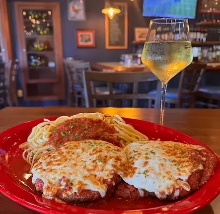 Spaghetti marinara, two cheesy parmesan dishes, and wine in a restaurant.