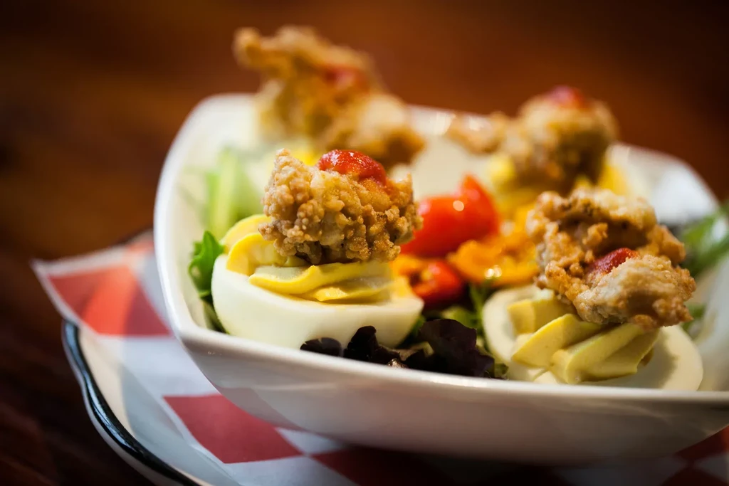 Deviled eggs topped with crispy fried food, red sauce, lettuce, tomatoes.